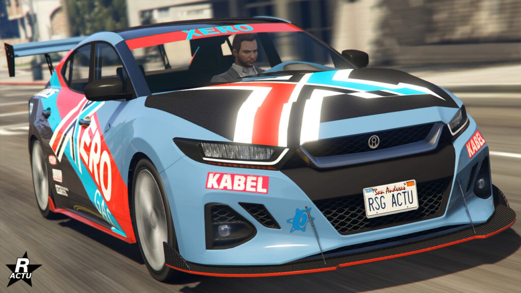 Vue de devant du véhicule Minimus de chez Annis dans le jeu Grand Theft Auto Online. Le bolide est peint en bleu ciel, a des décalcomanies de course, ainsi qu'un capot en carbone.