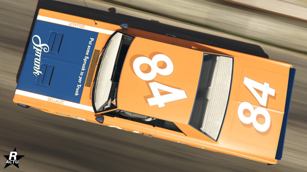 vue du dessus du véhicule américain Tampa GT. Sa peinture est en orange et sa carrosserie présente des décalcomanies de course, notamment le numéro "84" en grand sur le toit et le coffre.