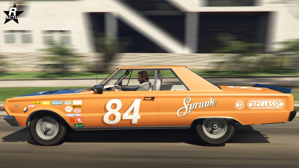 Vue latérale de la muscle car ancienne Tampa GT, elle est peinte en orange et a un motif de course avec divers autocollants, dont celui du numéro "84".