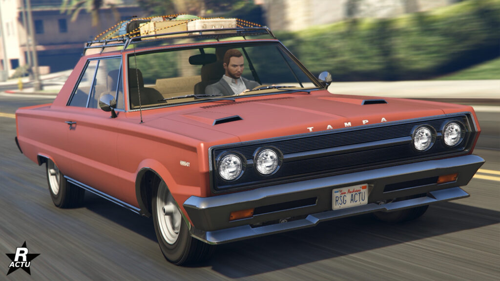 Bolide ancien Tampa GT sur une route ensoleillée du jeu vidéo Grand Theft Auto Online. Sa carrosserie est intégralement de couleur orange saumon et une grille de stockage avec des valises se trouve sur le toit.