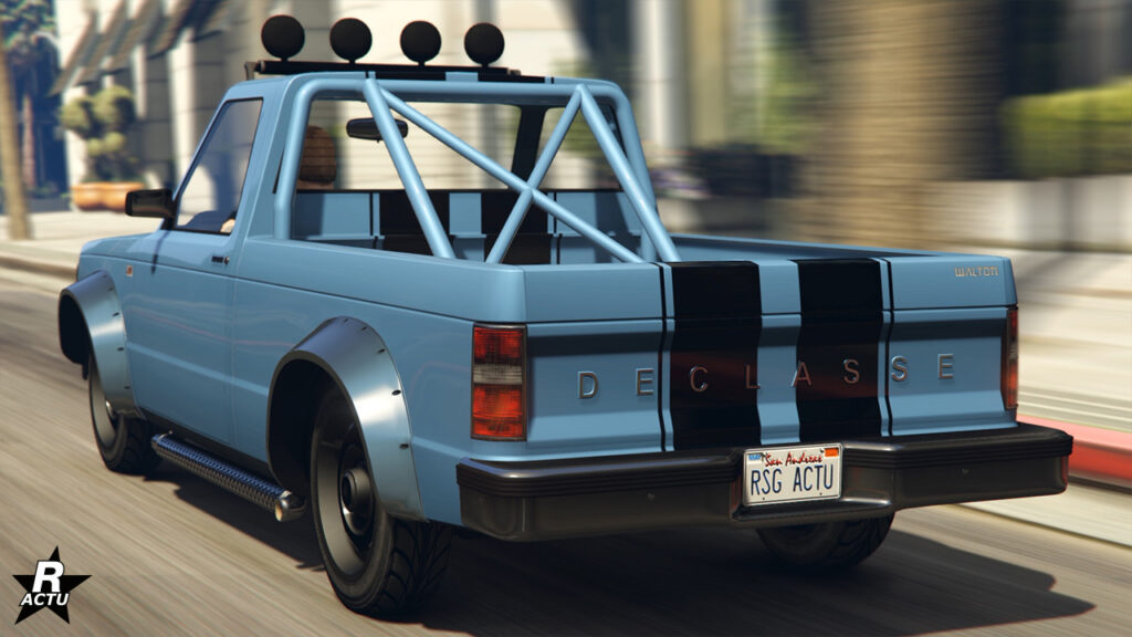 Face arrière du bolide tout-terrain "Declasse Walton L35 de série". Le Pick-Up des années 1980 est peint en bleu avec une double bande noire sur le rabattant. Des arceaux de sécurité sortent du plateau pour rejoindre le toit de la cabine surmonté de quatre projecteurs.