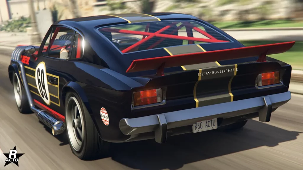 L'arrière du bolide de sport ancien Rapid GT Classique de chez Dewbauchee. La voiture de GTA Online est de couleur bleu nocturne aux nuances sombres. Sur le coffre et le toit, au centre, une décalcomanie d'une bande large grise horizontale, entourée d'une fine bande en or de chaque côté, est présente sur la carrosserie. Sur le coffre, un petit aileron rouge se trouve fixé. Tandis qu'à travers le pare-brise arrière, il est possible d'apercevoir des arceaux de sécurité rouge qui passent devant la vitre en forme d'une croix.