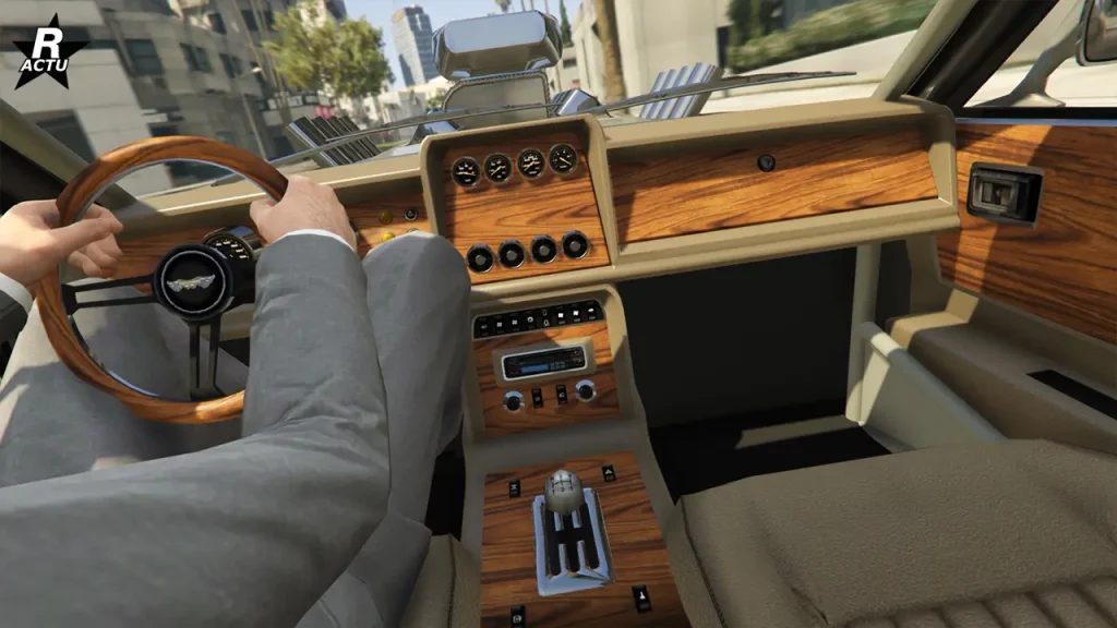 Image de l'habitacle de la voiture Rapid GT Classique d'un point du vue capturé depuis l'arrière de la console centrale qui est recouvert de boiserie vernis, tout comme les portières, le volant et les façades du tableau de bord. L'intérieur est raffiné et il est possible d'apercevoir le logo du constructeur, Dewbauchee, au centre du volant. Tandis que dans la console centrale, le manche à vitesses est chromé.