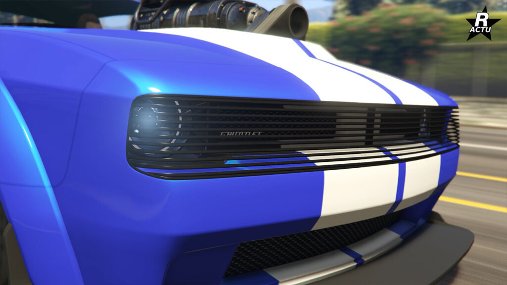 Vue rapprochée des phares avant où une grille noire horizontale les recouvres avec la calandre, la carrosserie est peinte en bleu électrique et une partie du bloc moteur dépassant du capot est visible.