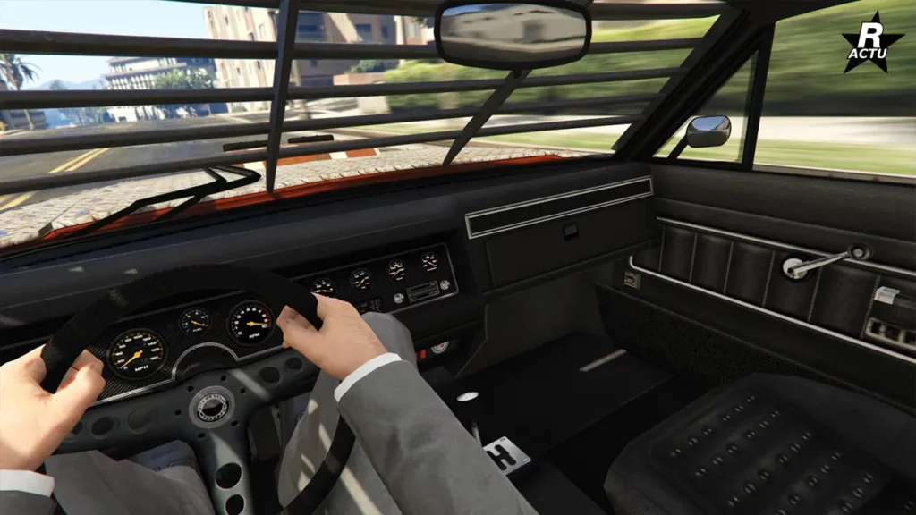 Point de vue du conducteur au volant de la Tampa armée. L'habitacle intérieur est assez sommaire, où un panneau en fibres de carbone se trouve derrière les compteurs analogiques du tableau de bord. La vue à travers le pare-brise est légèrement obstruée par un renforcement extérieur de lamelles horizontales.