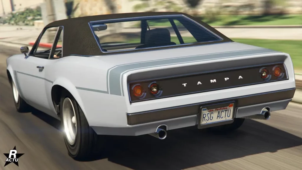 Image de l'arrière du muscle car Declasse Tampa sur une route du jeu Grand Theft Auto Online. La carrosserie est peinte en gris clair avec une fine bande grise foncée sur les cotés et une autre plus large sur le coffre. Le toit est recouvert d'une toile noire.