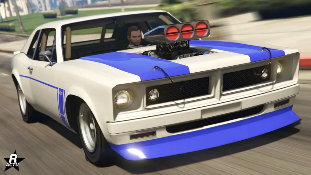 Vue avant de la grosse cylindrée Declasse Tampa dans le jeu vidéo GTA Online. La voiture américaine est peinte en blanche, avec des bandes violets sur le capot, où le bloc moteur dépasse.