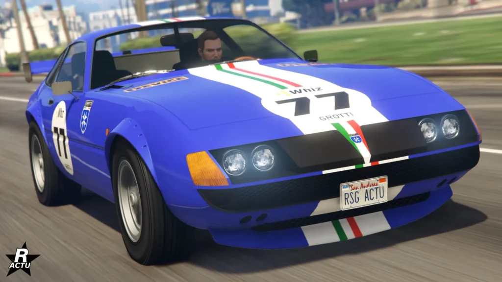 L'avant du véhicule de collection "Grotti GT750" sur une route de GTA Online. La carrosserie est peinte dans un bleu ultra avec une bande blanche incrustée du drapeau italien sur le capot.