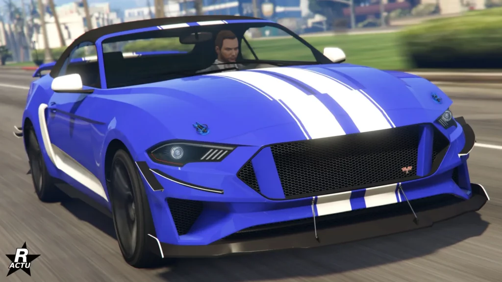 Image présentant la voiture américaine Vapid Dominator GT sur une route ensoleillée de GTA Online, avec une vue avant. Sa peinture en bleu et sa carrosserie dispose d'une décalcomanie d'une double bande blanche traversant verticalement le centre du capot. Sur les côtés latéraux, une autre bande blanche, cette fois horizontale, est présente.