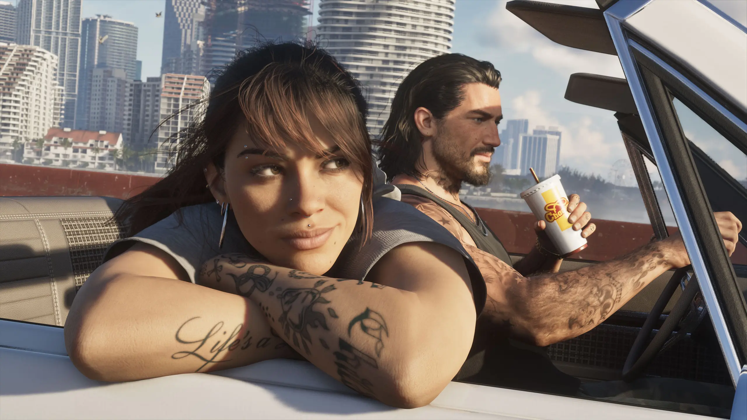 Jason et Lucia en balade dans une voiture décapotable dans GTA VI. Jason est au volant tout en tenant un gobelet de Fast-food, tandis que Lucia est accoudée sur la portière avec un regard rêveur.